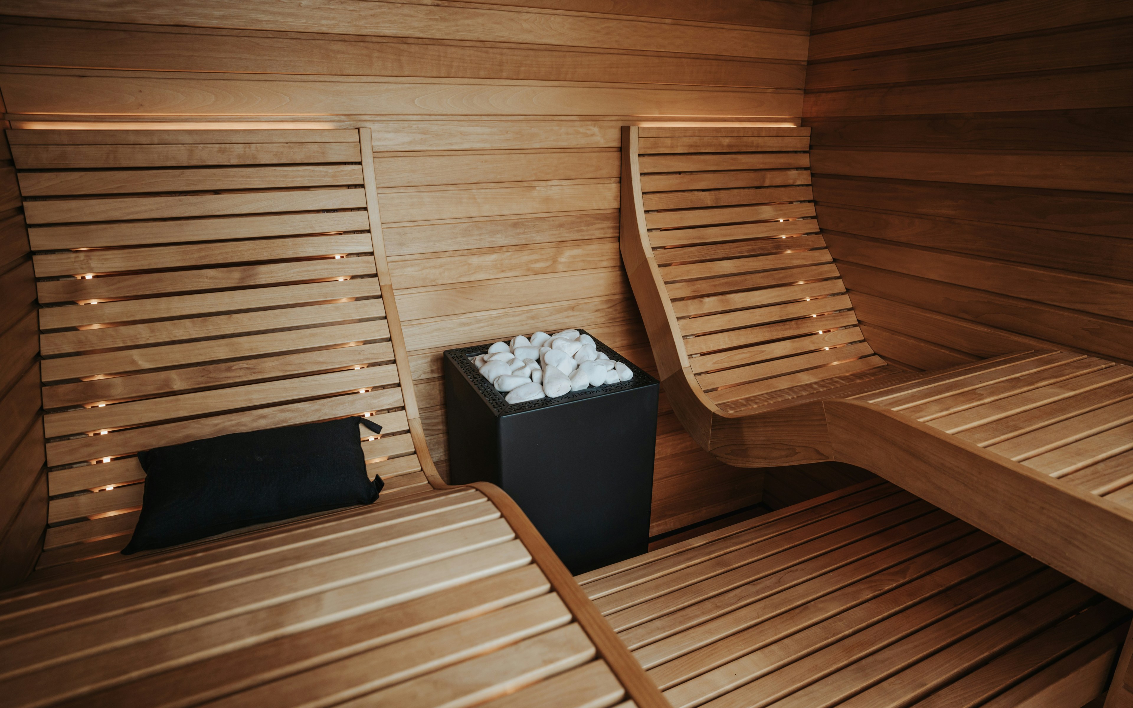 Interior de sauna de madera moderna con bancos y estufa, diseñado para la relajación y el rejuvenecimiento de la piel.