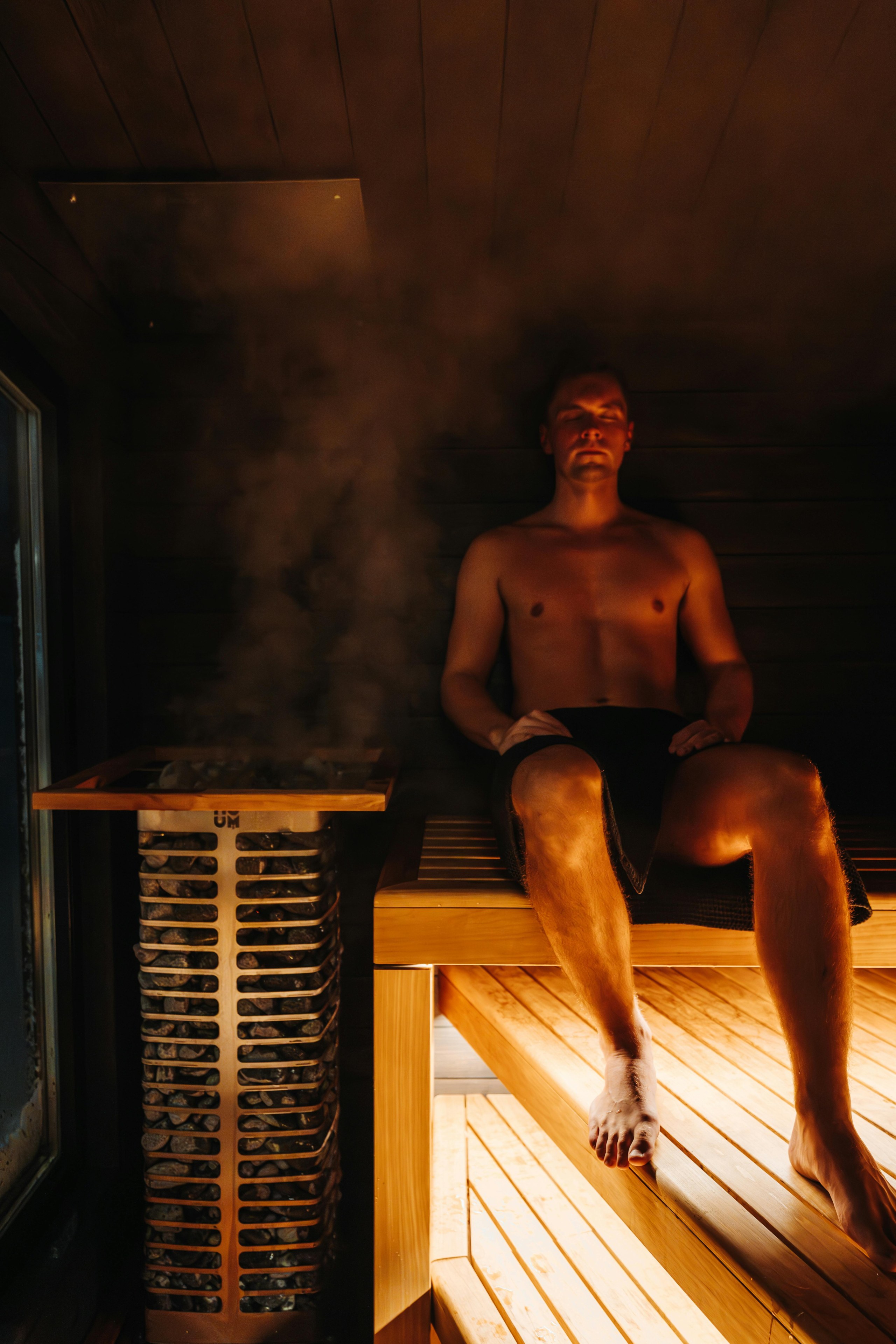 Un hombre se sienta en una sauna junto a un calentador de sauna humeante.