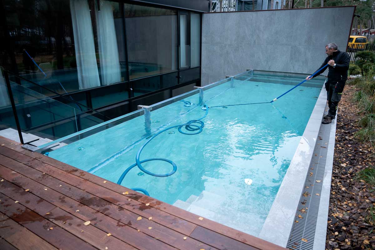 Una piscina con agua de color verde claro y turbia, la superficie cubierta por una capa de algas, una escena captada mientras una persona limpia la piscina.