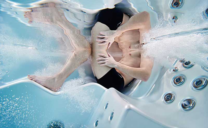 Mujer relajándose en una tumbona ergonómica de una piscina de spa USSPA con chorros de hidromasaje en funcionamiento.