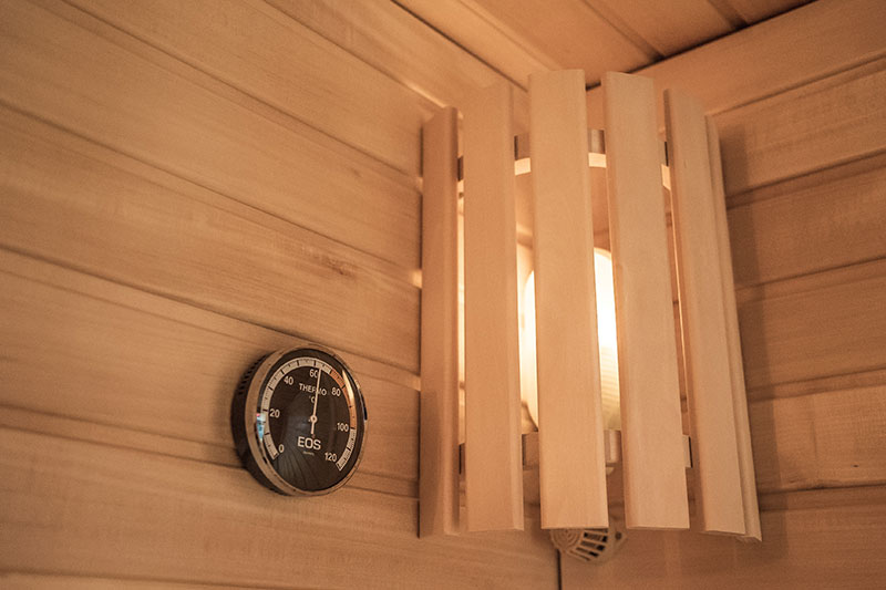 Termómetro de sauna EOS y pantalla de madera en la esquina.
