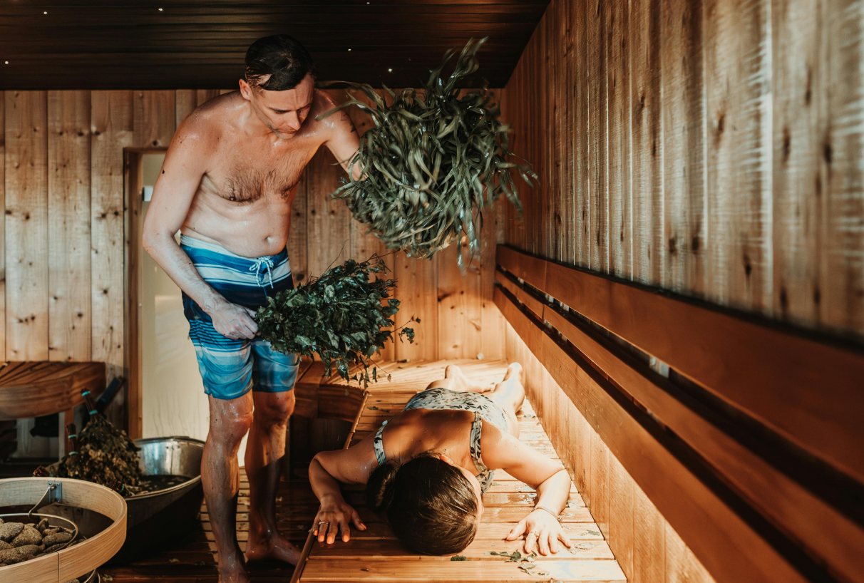 Un hombre está golpeando a una mujer con un látigo de abedul en la sauna, un ritual tradicional de la sauna para relajarse.